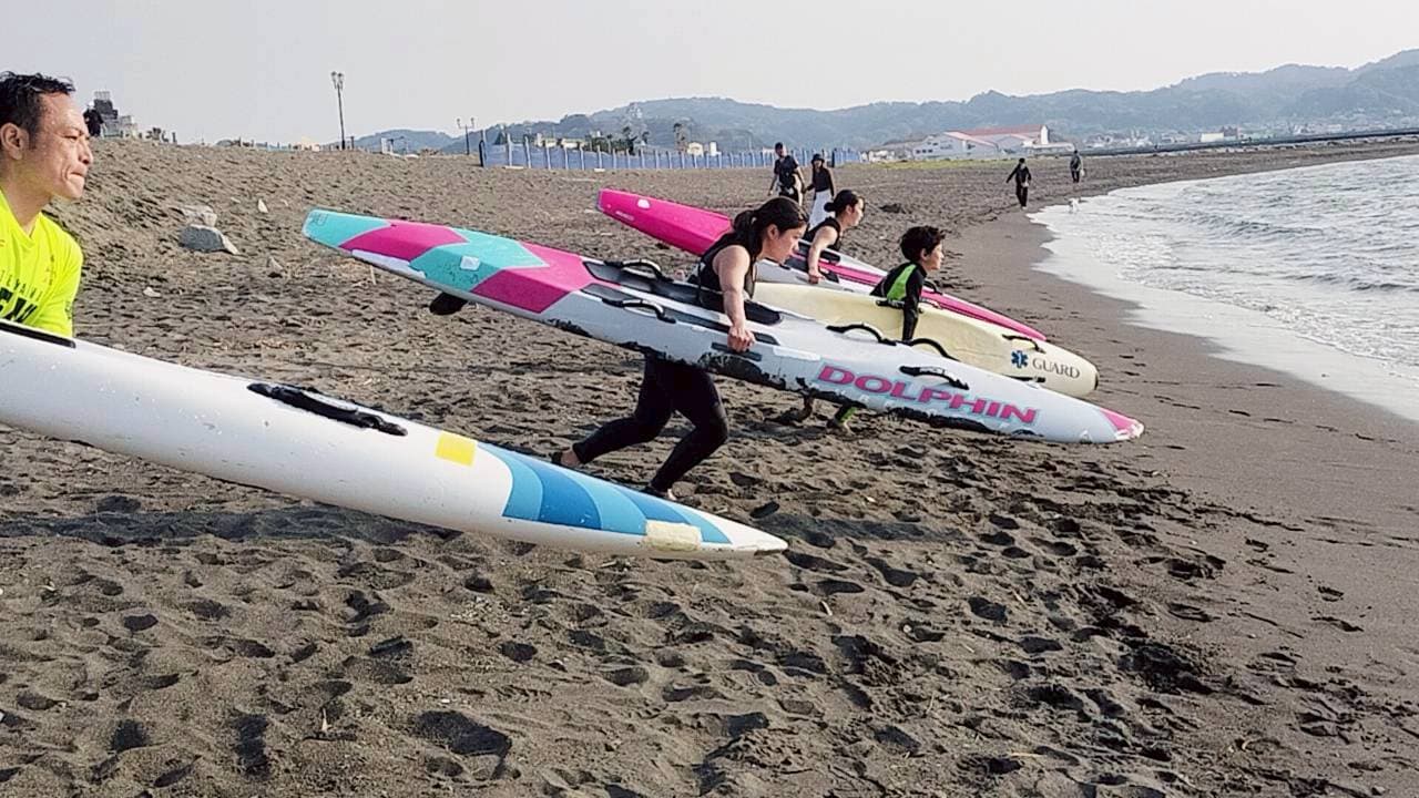 ビーチでボードを持って走るライフセーバーたち